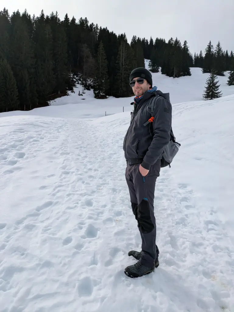 Ayal Othman standing on a snow-covered mountain path surrounded by forest, representing clarity, focus, and resilience.